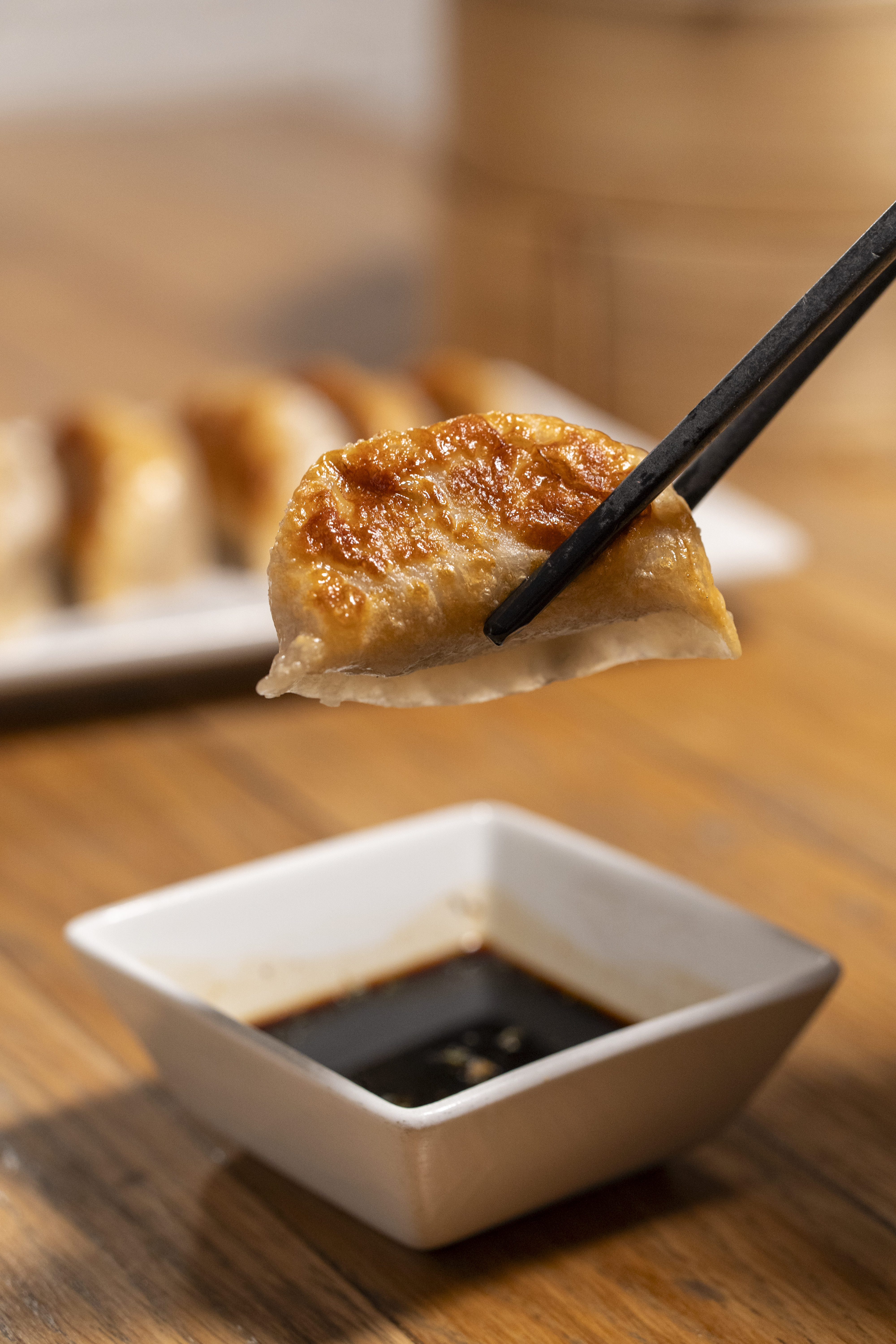 dumpling held over dipping sauce bowl
